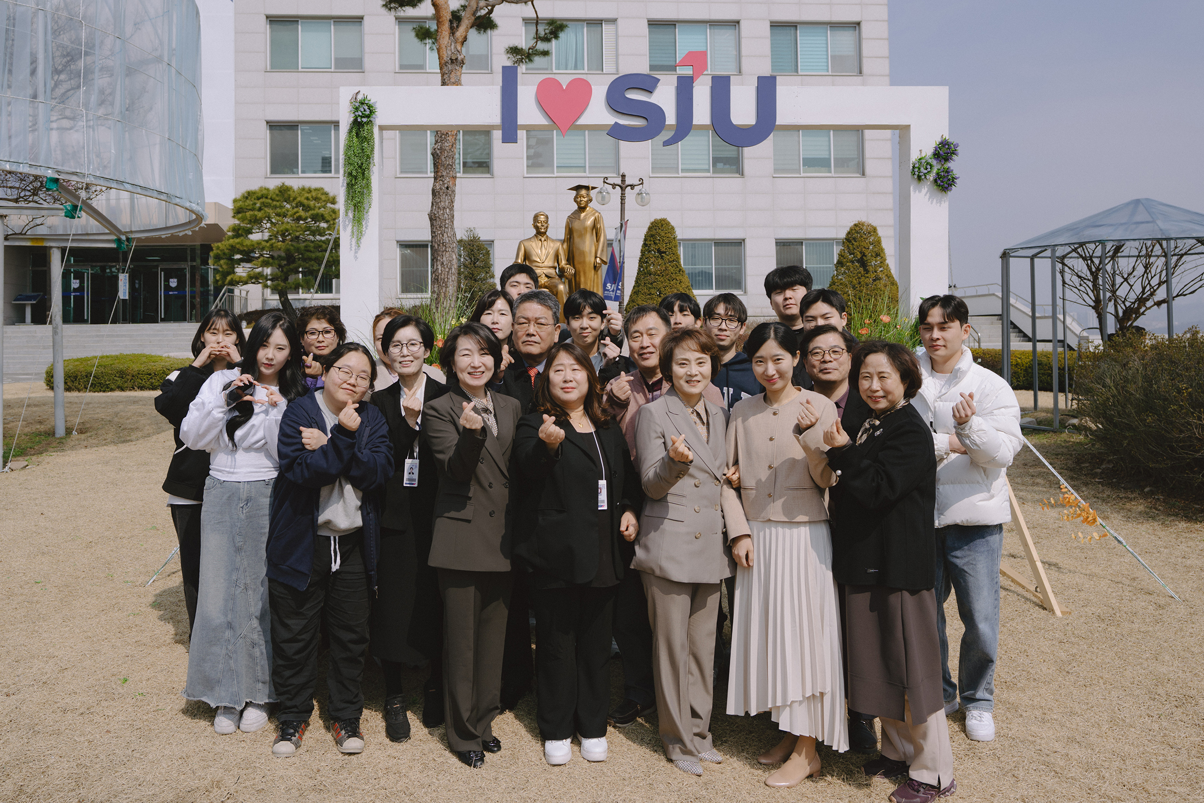 교수님과 학생들이 손가락 하트 포즈를 취하며, 단체사진을 찍고 있다.